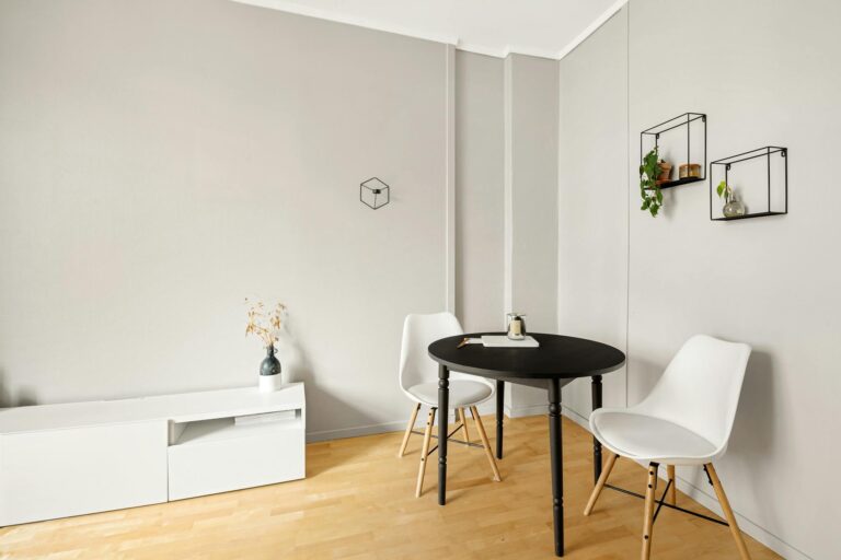 Elegant minimalist room featuring a black table, white chairs, and simple decor on light wood flooring.